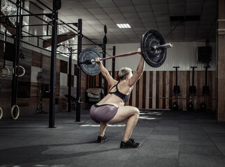 Fototapeta na wymiar Powerful and strong woman bodybuilder doing overhead with heavy barbell in modern cross gym. Functional training. Bodybuilding and Fitness