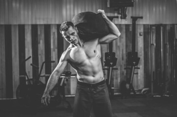 Fototapeta na wymiar Muscular male athlete exercising with heavy bag in modern cross gym. Functional training