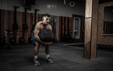 Fototapeta na wymiar Muscular male athlete exercising with heavy bag in modern cross gym. Functional training
