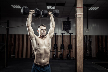 Powerful athletic man training shoulder muscles with heavy dumbbells doing overhead in gym. Healthy lifestyle concept