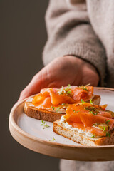 close up of woman holding white plate with smoked salmon toast as fresh snack, day light. Clean Eating. Healthy breakfast.