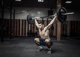 Muscular man practicing heavy barbell overhead at modern health club. Bodybuilding and Fitness