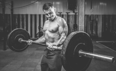 Muscular man with a naked torso training biceps with a heavy barbell in a modern health club. Bodybuilding and Fitness
