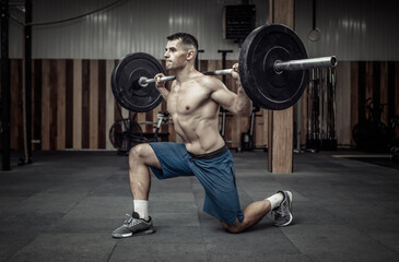 Young muscular male bodybuilder doing lunges with a barbell on his shoulders in a modern health...