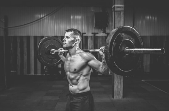 Portrait of a young muscular bodybuilder with a barbell on his shoulders in a modern health club