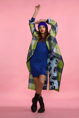 beautiful girl in a blue dress and a plaid coat, boots posing in the studio on a pink background
