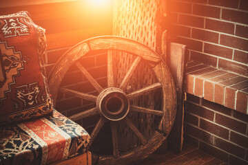 Detail ot Turkish mountain hut decoration. Wooden wheel, threshing board and a sofa covered with traditional anatolian rug near fire place. Warm sunlight coming from the window. 