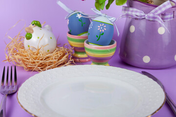 Easter table setting and dinner with yellow flowers, festive decorations, white bird and multicolored eggs.
