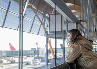 Naklejka premium Young blonde Caucasian Girl looks at the planes from a window at the airport when travelling
