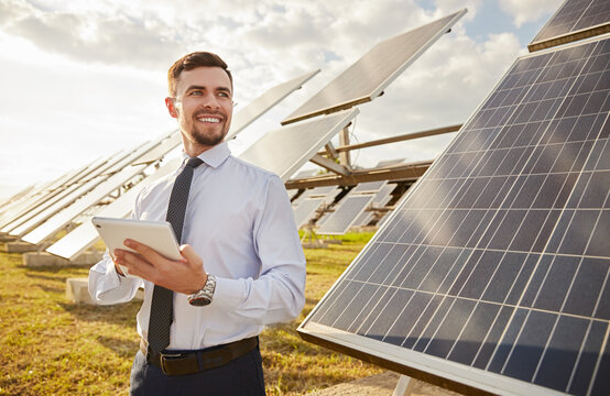 Cheerful businessman using tablet in meadow with solar batteries