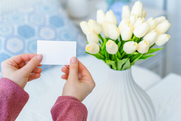 Woman pulling blank greeting card from bouquet of white tulips flowers. Mother day, Copy space. Mock up