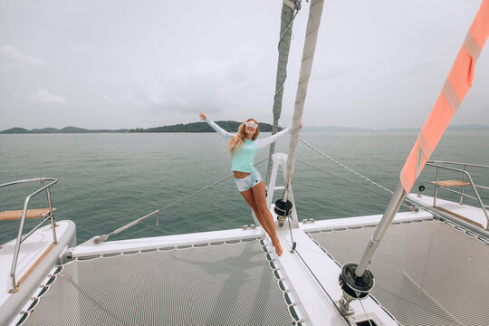 Tropical full-length photo of a happy smiling young beautiful girl with long blonde hair in a cute mint suit. Standing on the edge of the deck on a luxury white yacht with your hands held high.