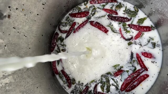 Pouring Milk Into Large Container With Herbs, Spices, And Chili Peppers. - vertical, high angle