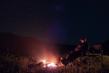 Man is resting near fireplace at night time with night sky