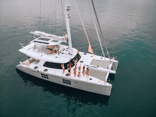 A bright and beautiful bird's-eye view picture of a white luxury-level yacht on the open sea. Young awesome girls in black and white swimsuits are enjoying the fun. The concept of the party.