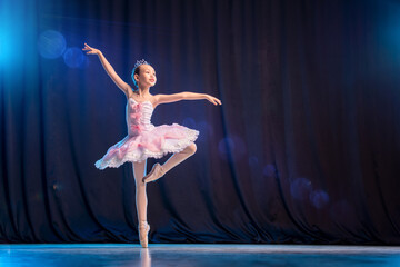 little girl ballerina is dancing on stage in white tutu on pointe shoes classic variation.