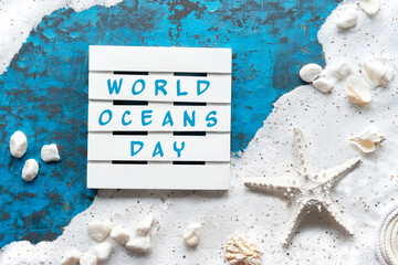 World Oceans Day text. Sand frame, seashells, starfish, cord. Text on white wooden palette....