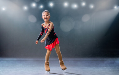 Little skater rides on rings in red and black dress on ice arena
