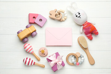 Baby shower party. Envelope surrounded by gift box and stuff for child on white wooden background, flat lay