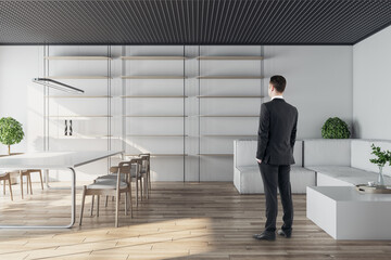 Businessman standing in modern conference room interior with glass partition, wooden flooring and daylight. Workplace concept.