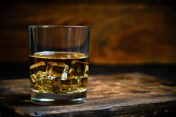 Glass chilled whiskey with ice cubes on wooden background in cellar.