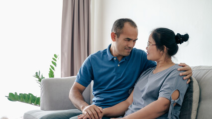 Portrait of Asian mature couple sitting in the living room. wife and husband hugging, holding hand...
