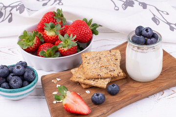 Healthy breakfast with homemade yoghurt and fresh strawberries and blueberries, whole grain bread on a white wooden table in rustic style, close up, horizontal