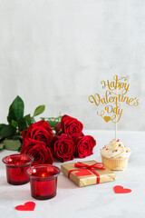 St. Valentine's Day present. Small hearts, candles, a gift box, a cupcake and red roses bouquet on light background. Romantic love background. Happy Valentines Day. Greeting card, poster. Copy space