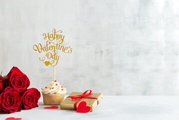 Cupcake with vanilla cream and red sugar hearts for St. Valentine's Day and roses bouquet with a gift on light background. Recipe, Romantic gift. Bakery, confectionery menu, greeting card. Copy space