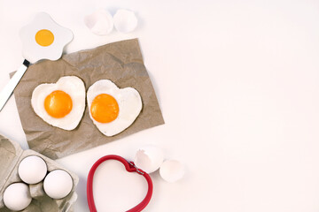 Heart shaped fried eggs served on craft paper, white background, flat lay, copy space. 
Valentines day breakfast idea. 