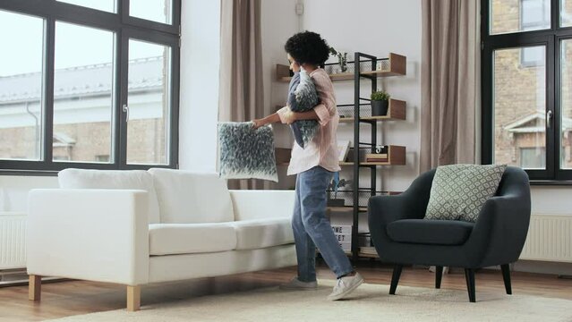household, home improvement and cleaning concept - woman arranging cushions on armchair and sofa