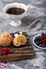 Small white buns with fresh berries with cup of coffee on a concrete texture background