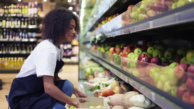 Curly female arranging big green apples on shelf