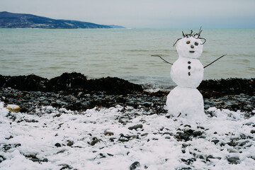 a snowman in the southern city stands on a stone beach by the sea