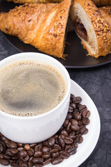 Breakfast consisting of fresh croissant with chocolate and coffee in white cup