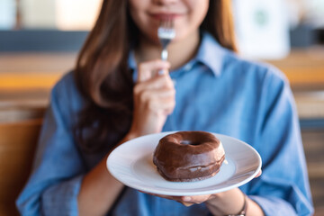 Closeup image of a young woman holding and eating chocolate donut