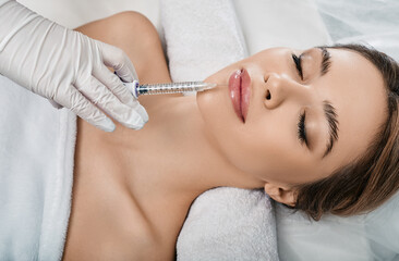 Woman while procedure lip augmentation at cosmetology clinic with beautician. Filler injection for...