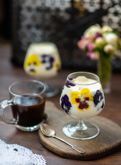 Dessert in a glass with fresh pansy flowers inside on a wooden background