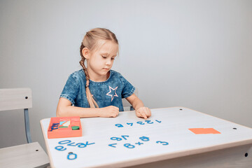 Portrait of a focused intelligent cool child sitting at a white table with numbers in the correct order and a girl pointing to the numbers, memorizing them. Development process. Study concept. 