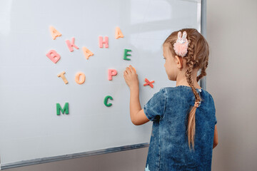 Portrait of a focused intelligent lovely kid standing in front of a white board with alphabet...