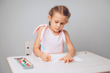 Portrait of a talanted lovely pretty kid sitting at a table and drawing on paper with crayons. Drawing concept. photo with noise