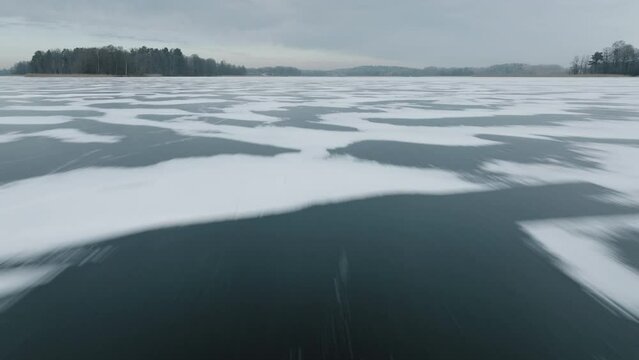 Frozen Lake with snow patterns from low wide angle fast flying Mavic 3 Cine drone. Filmed in prores at 50fps. Winter daytime. Ice clouds ant trees in horison visible.