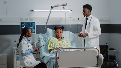 Obraz premium Team of doctors talking about disease diagnosis with patient in hospital ward. Man and woman giving medical help and assistance to sick person in bed. Healthcare workers healing adult