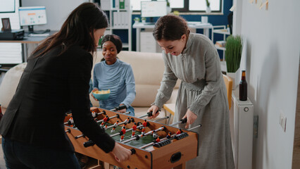 Corporate workmates using foosball table to play soccer game, playing after work at office....
