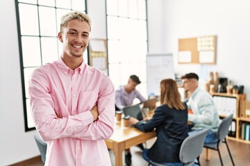 Young hispanic businessman smiling happy standing with arms crossed gesture at the office during business meeting.