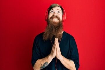 Redhead man with long beard listening to music using headphones begging and praying with hands together with hope expression on face very emotional and worried. begging.