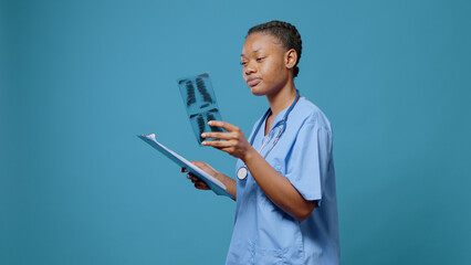 African american nurse analyzing radiography in studio. Medical assistant looking at x ray scan in hand to find diagnosis and healthcare treatment. Woman with expertise having results