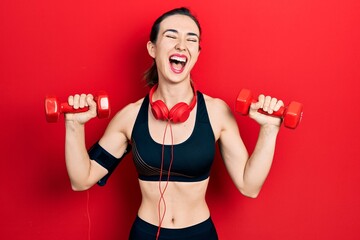 Young hispanic girl wearing sportswear using dumbbells and headphones smiling and laughing hard out loud because funny crazy joke.