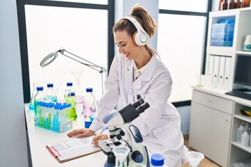 Young woman wearing scientist uniform listening to music writing report at laboratory