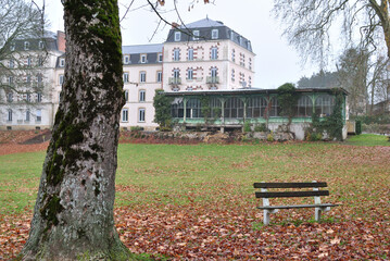 Empty Bench in Grassy Public Park with Old Hotel and Trees